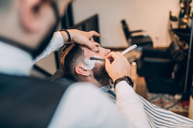 Jonge knappe hipstermens die kapperswinkel bezoekt. Trendy en stijlvolle baard styling en snit.