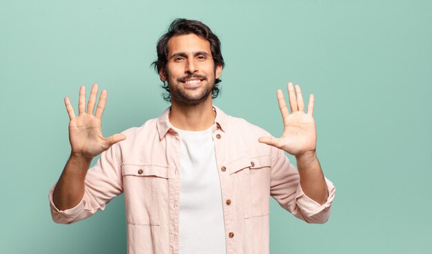 Jonge knappe Indiase man die lacht en er vriendelijk uitziet, nummer tien of tiende toont met de hand naar voren, aftellend