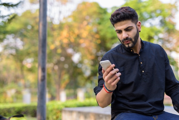 Jonge knappe Indische mens die mobiele telefoon met behulp van terwijl