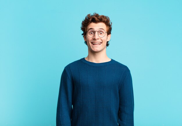 Jonge knappe jongen die er blij en aangenaam verrast uitziet, opgewonden met een gefascineerde en geschokte uitdrukking