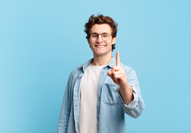 Jonge knappe jongen die trots en zelfverzekerd glimlacht en nummer één triomfantelijk poseert