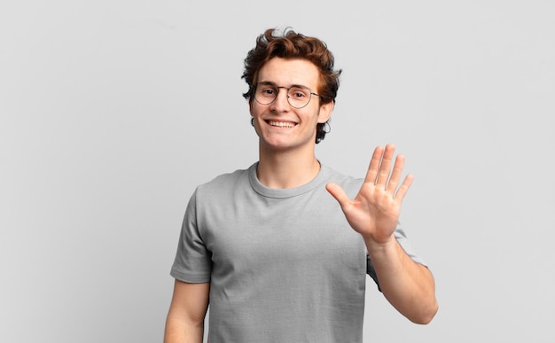 Jonge knappe jongen die vrolijk en opgewekt lacht, met de hand zwaait, je verwelkomt en begroet, of afscheid neemt