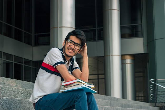 Jonge knappe jongen glimlacht en zit met boeken op de trap