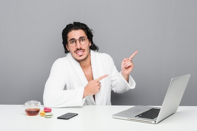 Jonge knappe man aan het werk na een douche geschokt wijzend met wijsvingers naar een kopie ruimte