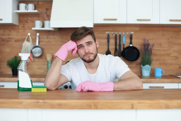 Jonge knappe man denkt na over de noodzaak om de keuken schoon te maken.