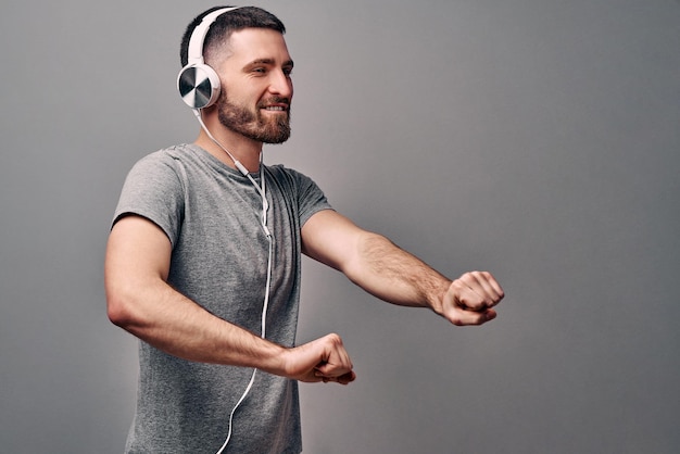 jonge knappe man die danst op zijn favoriete muzieknummer, gekleed in een grijs t-shirt en een witte koptelefoon