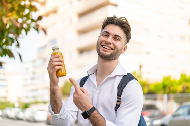 Jonge knappe man die een jus d'orange naar buiten houdt en erop wijst