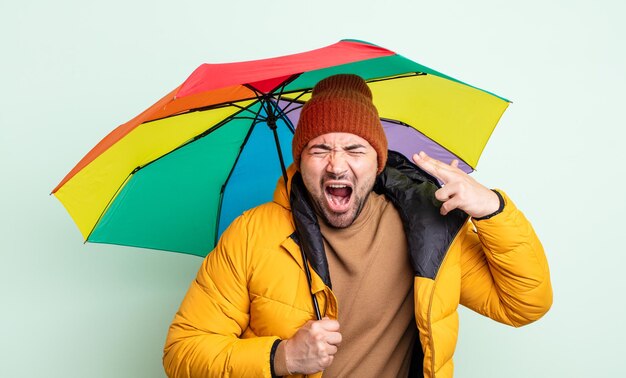 Jonge knappe man die er ongelukkig en gestrest uitziet, zelfmoordgebaar dat een pistoolteken maakt. regen en paraplu concept