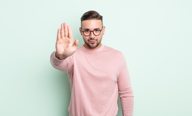 Jonge knappe man die er serieus, streng, ontevreden en boos uitziet en een open palm laat zien die een stopgebaar maakt