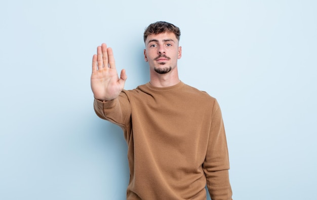 Jonge knappe man die er serieus, streng, ontevreden en boos uitziet met een open palm die een stopgebaar maakt