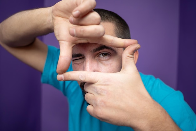 Foto jonge knappe man die frame maakt met zijn handen, handpalmen en vingers op een paarse achtergrond