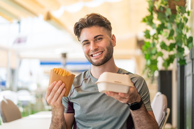 Jonge knappe man die gebakken frites en afhaalmaaltijden neemt met een gelukkige uitdrukking