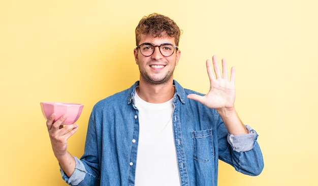 Jonge knappe man die lacht en er vriendelijk uitziet, met nummer vijf. lege kom concept