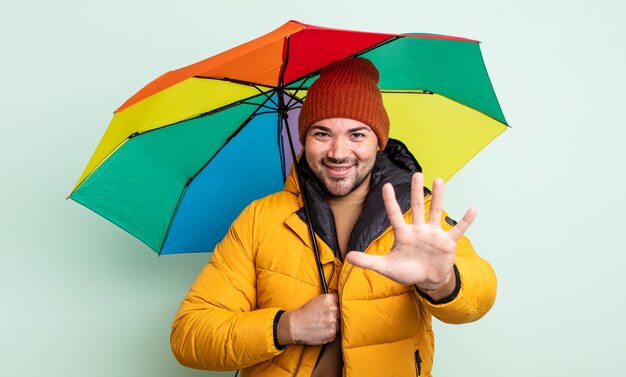 Jonge knappe man die lacht en er vriendelijk uitziet, met nummer vijf. regen en paraplu concept