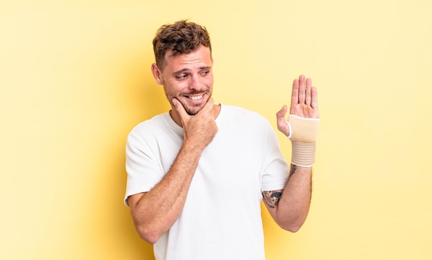 Jonge knappe man die lacht met een gelukkige, zelfverzekerde uitdrukking met de hand op de kin. handverband concept