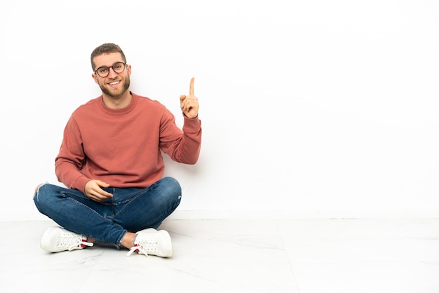 Jonge knappe man die op de grond zit en een vinger opsteekt als teken van het beste?