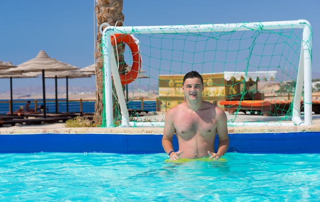 Jonge knappe man die op een zonnige zomerdag bij de poort in het zwembad waterpolo speelt in het hotel