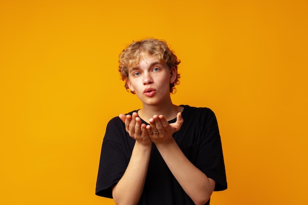 Jonge knappe man die over een gele achtergrond staat en naar de camera kijkt en een kus met de hand blaast