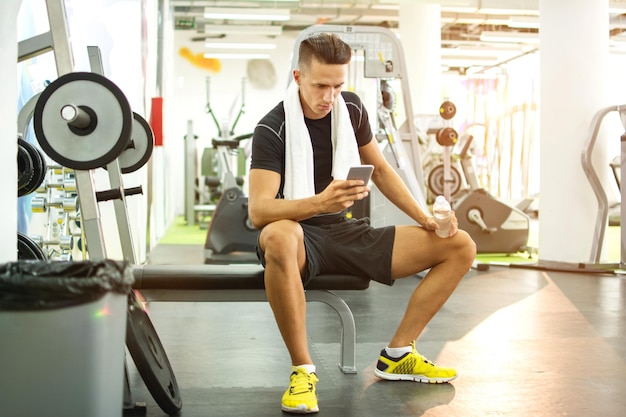Jonge knappe man die telefoon gebruikt tijdens een oefenpauze in de sportschool