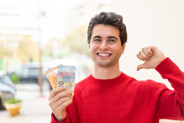 Jonge knappe man die veel geld meeneemt naar buiten, trots en zelfvoldaan