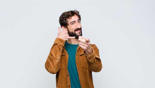 Jonge knappe man die vrolijk glimlacht terwijl hij je later belt, praat aan de telefoon tegen een vlakke muur