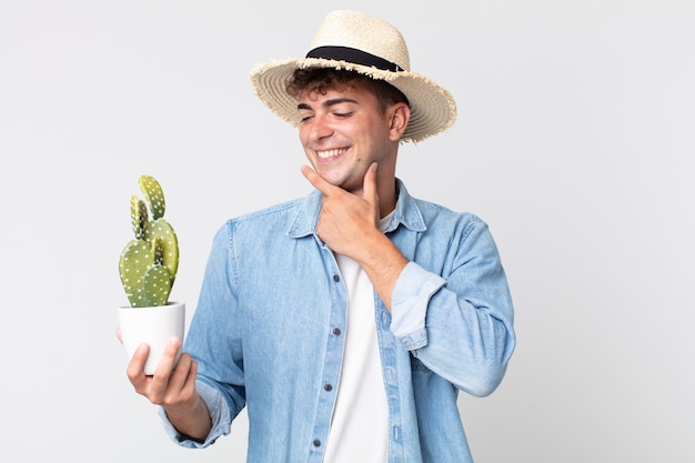 Jonge knappe man die vrolijk lacht en dagdroomt of twijfelt. boer met een decoratieve cactus