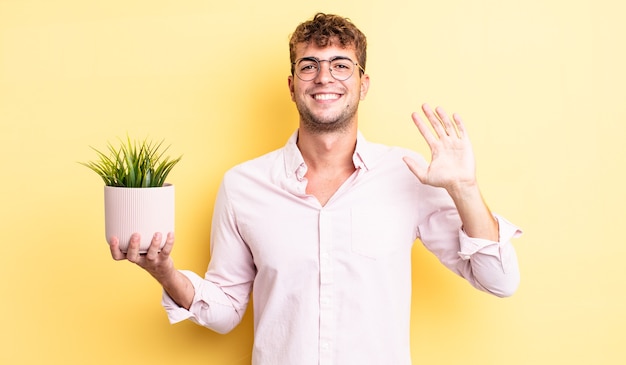 Jonge knappe man die vrolijk lacht, met de hand zwaait, je verwelkomt en begroet. decoratief plantenconcept