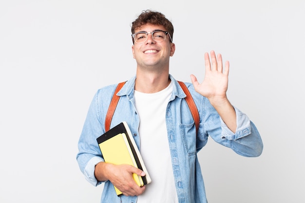 jonge knappe man die vrolijk lacht, met de hand zwaait, je verwelkomt en begroet. universitair studentenconcept