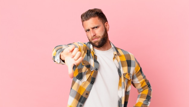 jonge knappe man die zich boos voelt en duimen naar beneden laat zien