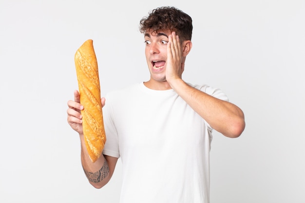 Jonge knappe man die zich gelukkig, opgewonden en verrast voelt en een stokbrood vasthoudt