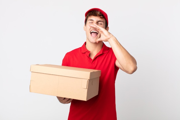 Jonge knappe man die zich gelukkig voelt, een grote schreeuw uitdeelt met handen naast het concept van de leveringspakketdienst.
