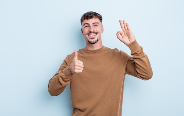 Jonge knappe man die zich gelukkig voelt, verbaasd, tevreden en verrast, oke tonen en duimen omhoog gebaren glimlachen