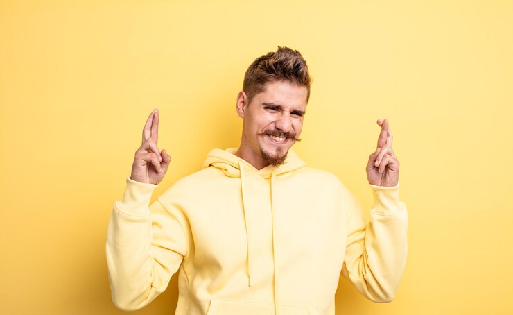 Foto jonge knappe man die zich nerveus en hoopvol voelt en vingers kruist, biddend en hopend op geluk, vreemd snorconcept