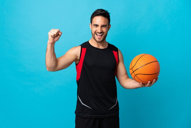 Jonge knappe man geïsoleerd op blauw basketbal spelen