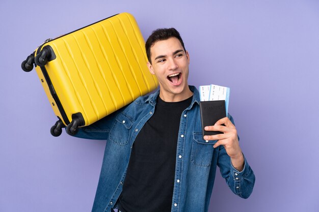 Jonge knappe man geïsoleerd op paarse muur in vakantie met koffer en paspoort