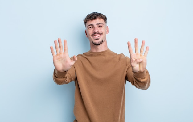 Jonge knappe man glimlachend en vriendelijk kijkend, nummer negen of negende tonend met de hand naar voren, aftellend