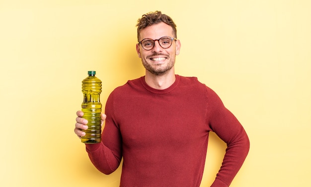 Jonge knappe man glimlachend gelukkig met een hand op de heup en zelfverzekerd. olijfolie concept