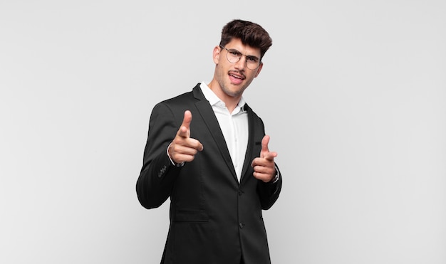 Jonge knappe man glimlachend met een positieve, succesvolle, gelukkige houding wijzend naar de camera, pistool teken met handen maken