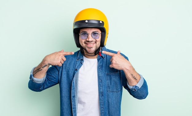 Jonge knappe man glimlachend vol vertrouwen wijzend naar eigen brede glimlach motorhelm concept