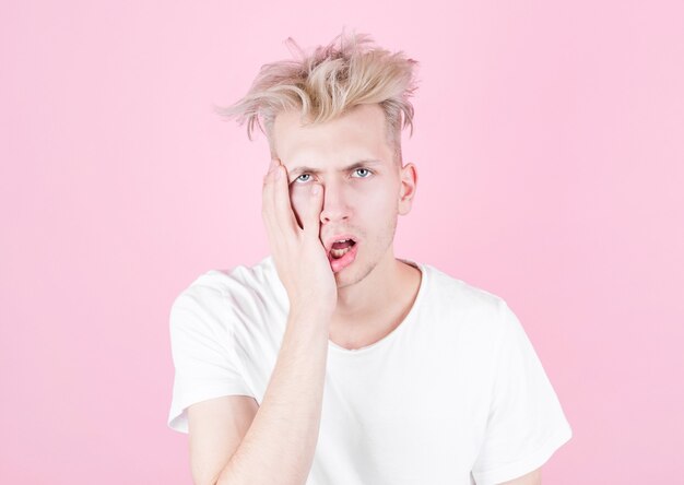 Jonge knappe man in een wit T-shirt is moe en wil slapen. Ondersteunt zijn gezicht met zijn hand om wakker te blijven. Slaap, vermoeidheid en stress concept.