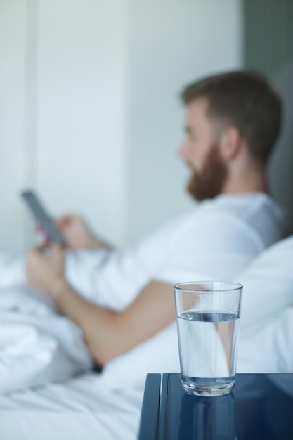 Jonge knappe man in het bed in de slaapkamer thuis in de ochtend ligt onder een witte deken en