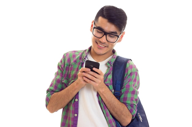 Jonge knappe man in wit T-shirt en geruit overhemd met blauwe rugzak met zijn smartphone