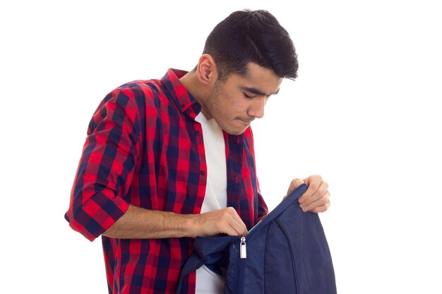 Jonge knappe man in wit T-shirt en rood geruit overhemd op zoek naar zijn blauwe rugzak