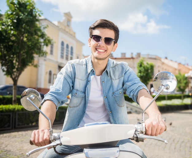 Jonge knappe man in zonnebril rijden scooter.