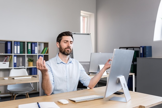 Jonge knappe man kantoormedewerker zit aan een computerbureau die zich moe uitrekt om een pauze te nemen en yoga-oefeningen te doen, rustend