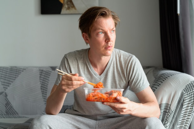 Jonge knappe man kimchi eten en denken in de huiskamer