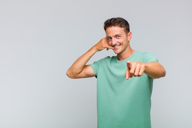 Jonge knappe man lacht vrolijk en wijst naar de camera terwijl je later belt, telefoneert