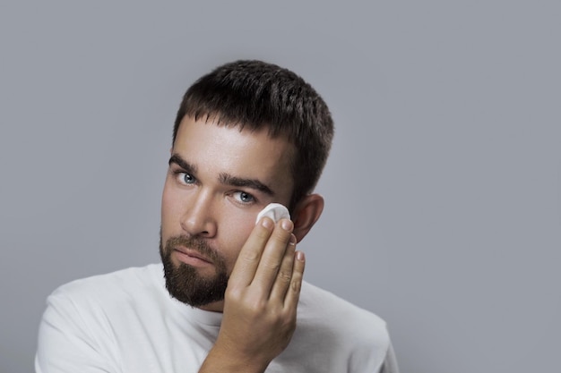 Jonge knappe man maakt zijn gezicht schoon met een wattenschijfje