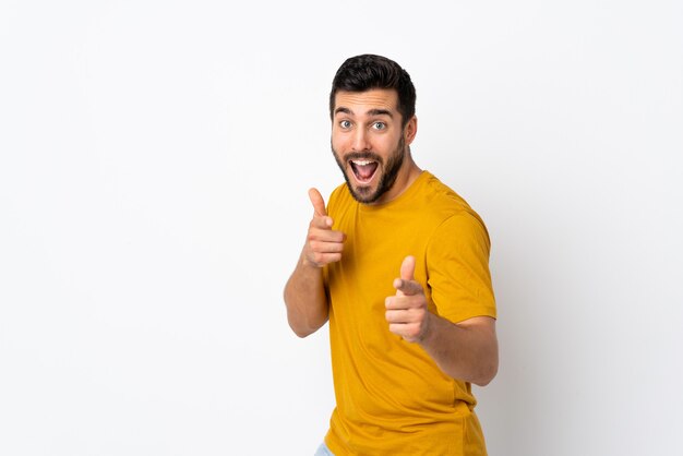 Jonge knappe man met baard geïsoleerd op een witte muur naar voren wijzen en glimlachen