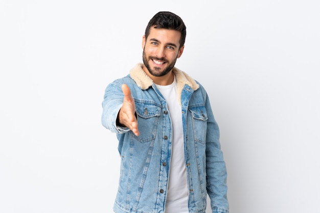 Jonge knappe man met baard geïsoleerd op witte muur handen schudden voor het sluiten van een goede deal